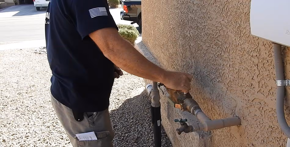 Person adjusting an outdoor water meter valve attached to a stucco wall.