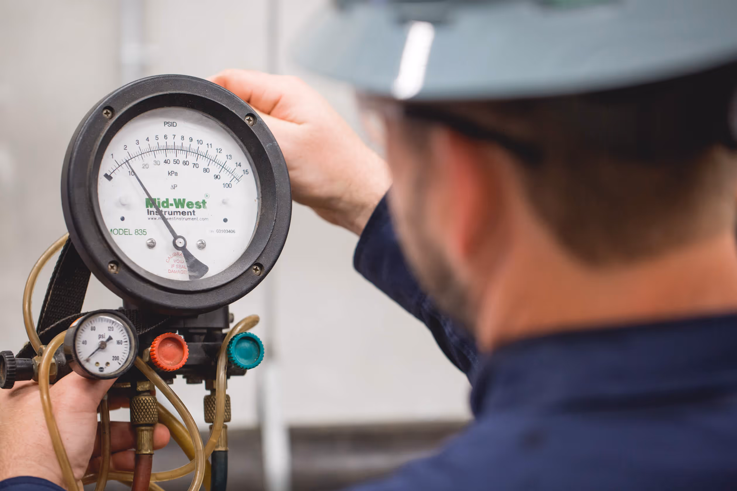 Technician wearing a hard hat adjusting a Mid-West Instrument pressure gauge with connected tubes.
