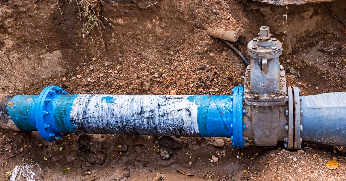 Blue metal pipeline with a valve partially buried in dirt and mud.