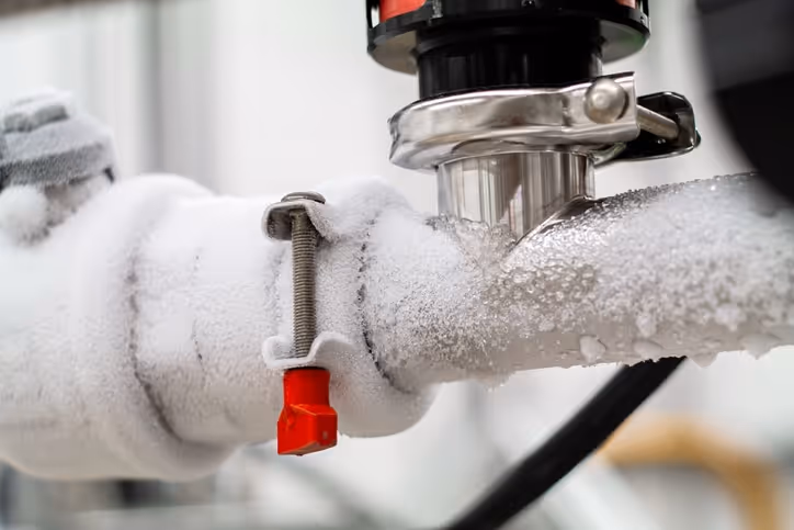 Close-up of an industrial pipe covered in frost with a red valve handle and metal fittings.