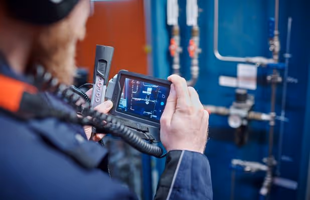 Technician using a handheld thermal imaging camera to inspect industrial piping.