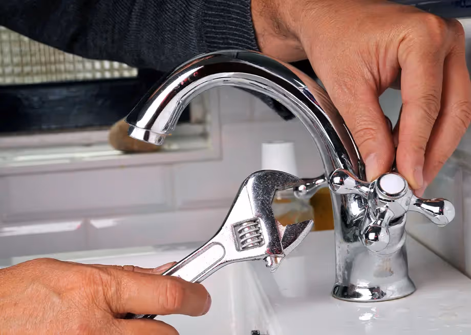 Person using an adjustable wrench to fix a chrome faucet in a bathroom sink.
