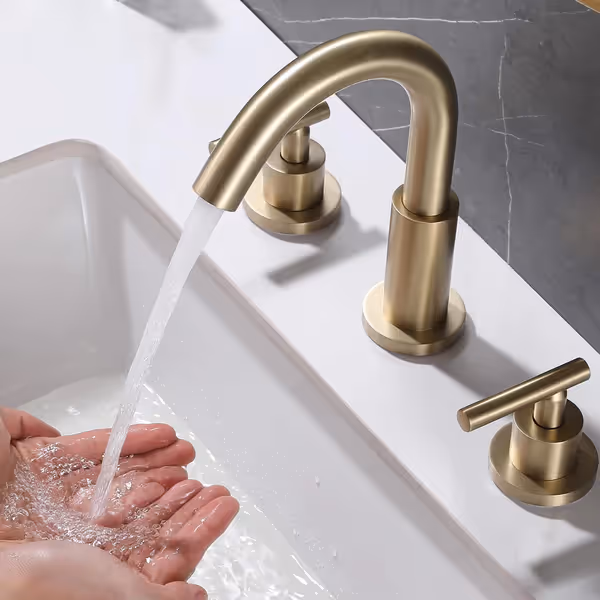 Brushed gold faucet with running water over cupped hands above a white sink.