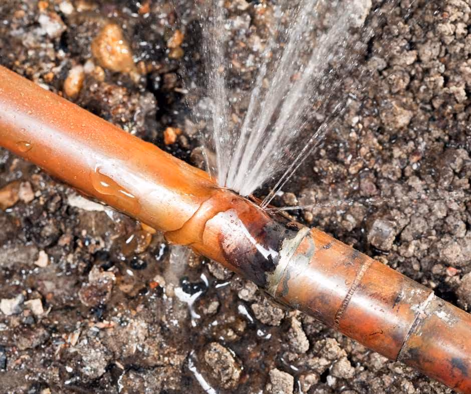 Copper pipe leaking water through a burst section above soil.