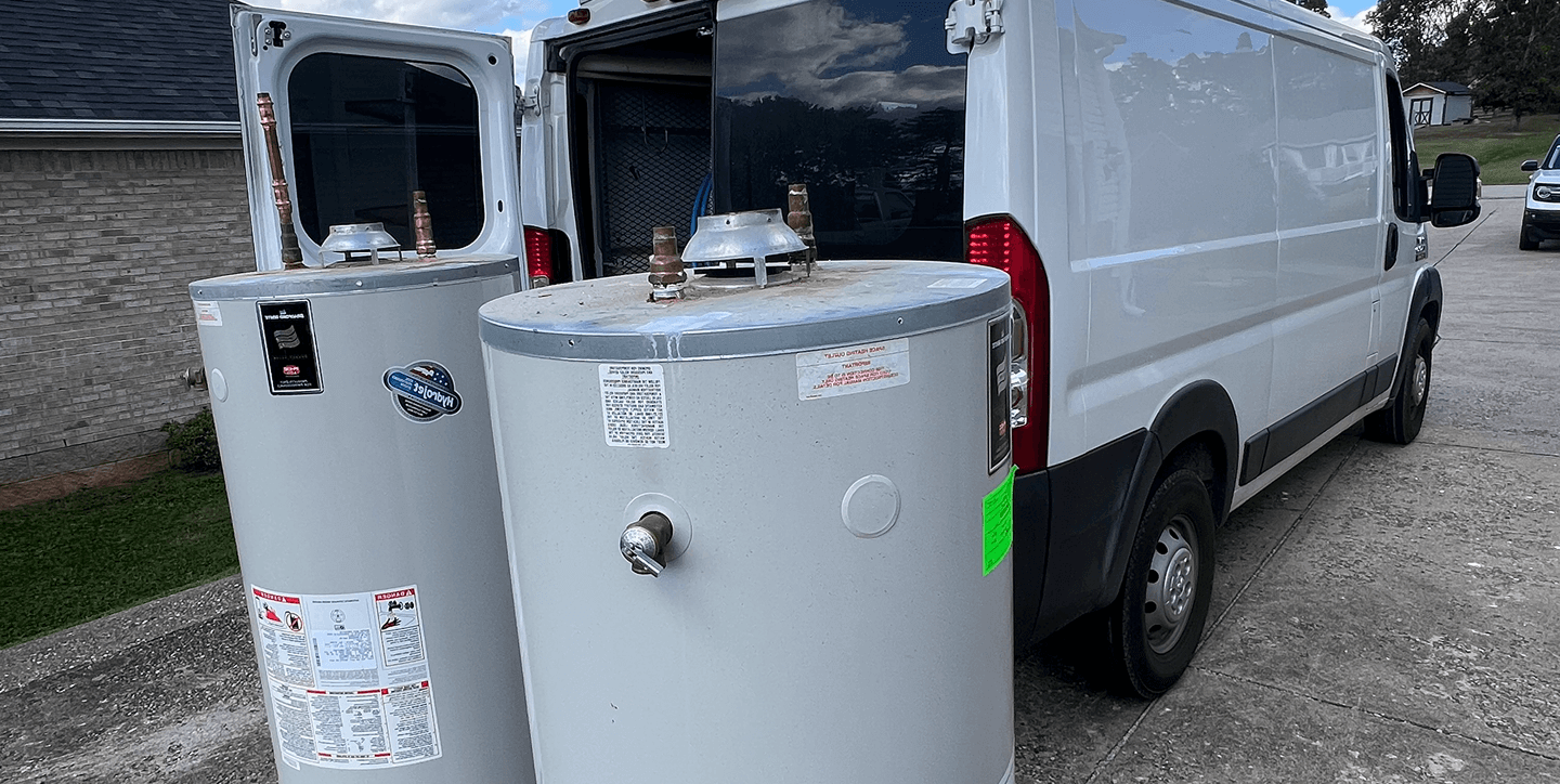 Two large water heaters placed next to a white service van on a concrete driveway.