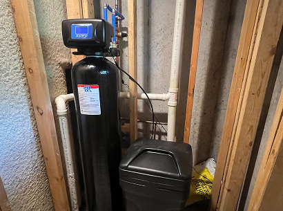 Water softener system installed in a wooden framed basement wall with pipes connected.