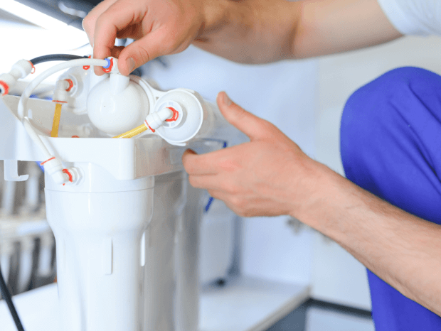 Person assembling or maintaining a white water filtration system with connected tubes and fittings.