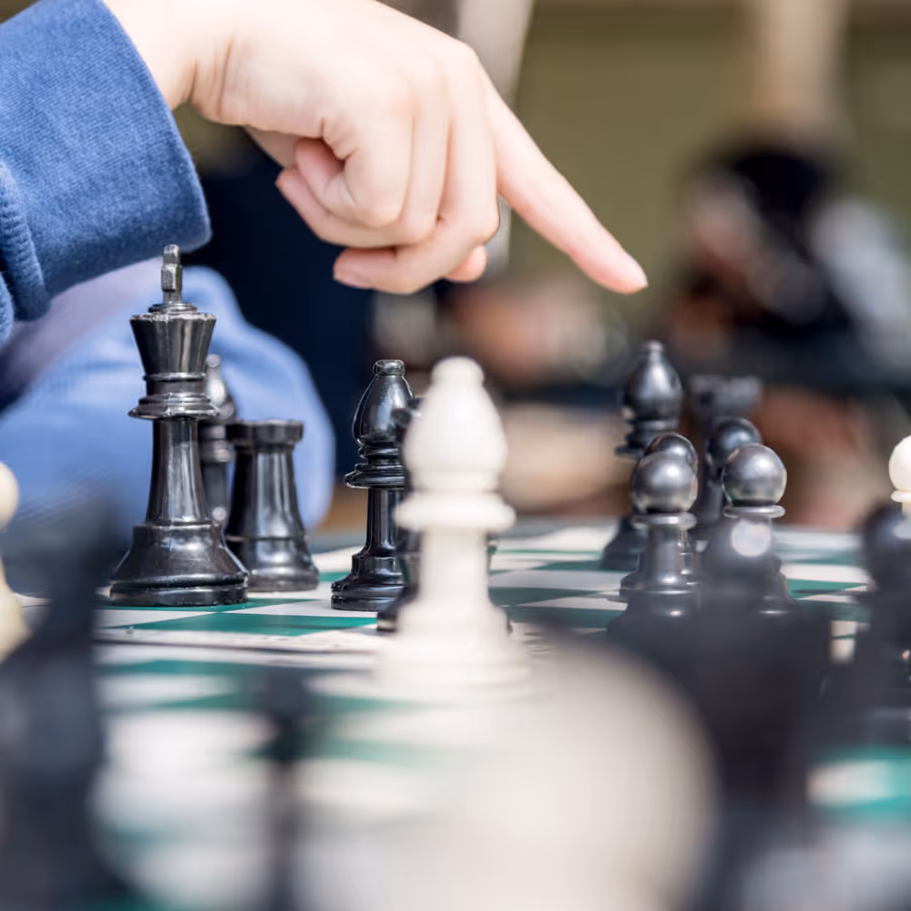Hand pointing at black chess pieces on a chessboard during a game.