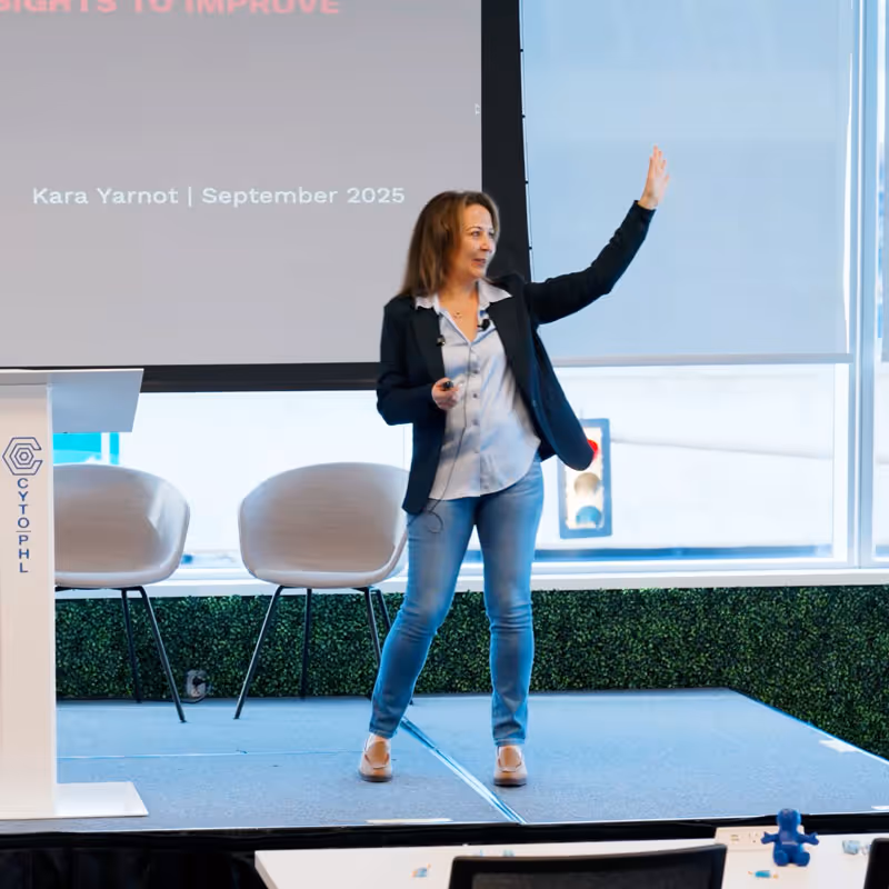 Kara Yarnot standing on stage with one hand raised during a presentation.