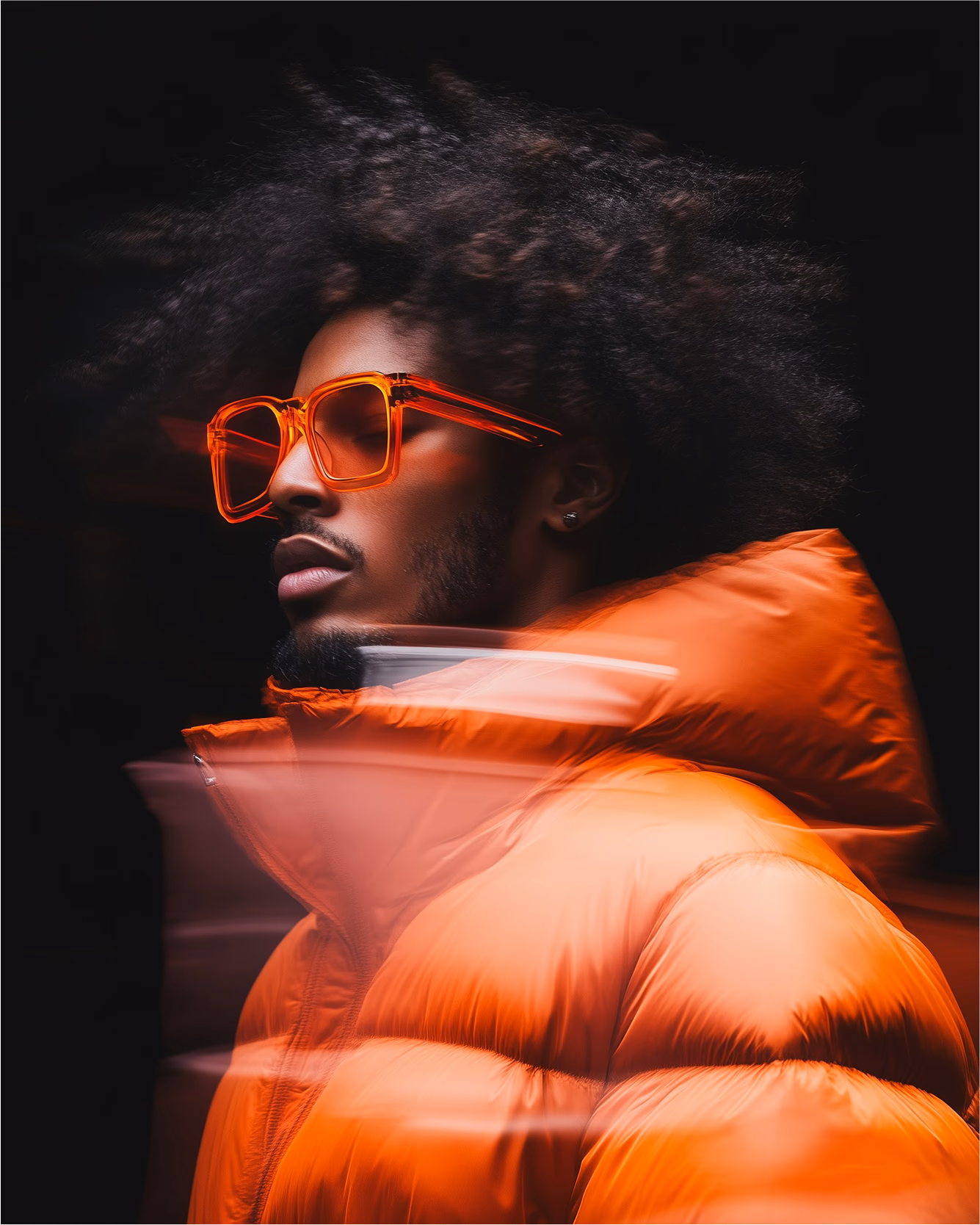 Portrait of a man with curly hair wearing large orange sunglasses and an orange puffer jacket against a dark background with motion blur effects.