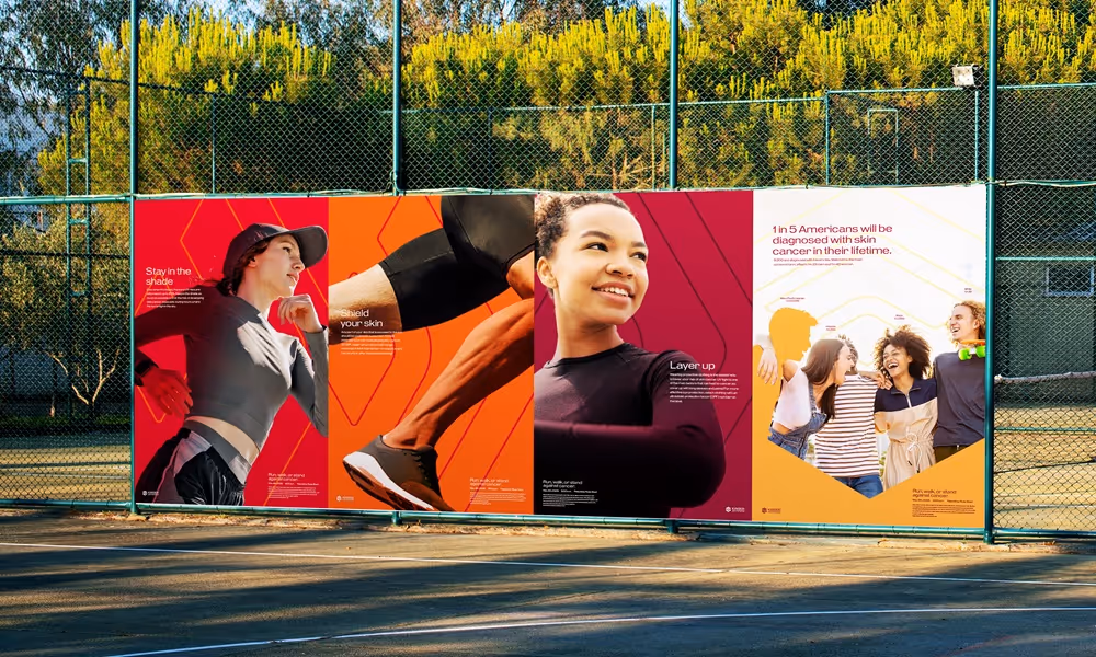 Four promotional posters in front of a tennis court. The posters are informing people about how to prevent skin cancer.