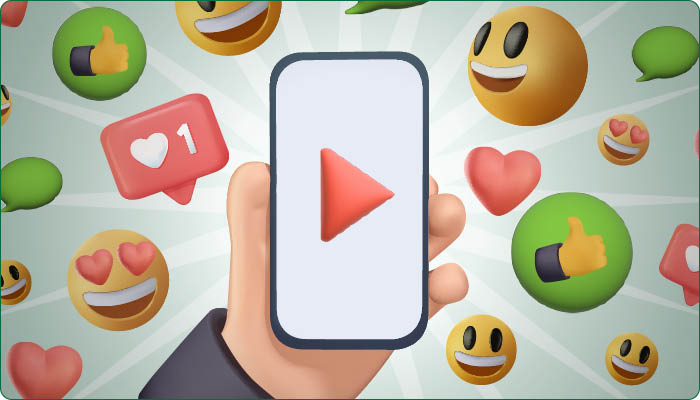 A hand holds a smartphone displaying a play button. Surrounding it are various emojis, including smiley faces, hearts, and thumbs-up icons.