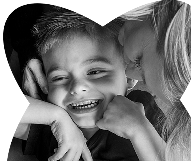 Smiling young boy embraced and kissed gently on the cheek by a woman with long hair.
