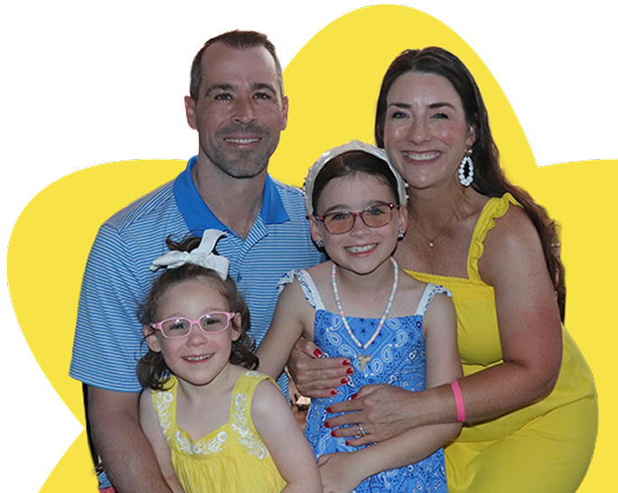 Smiling family of four with two young girls wearing glasses and bright summer clothing.