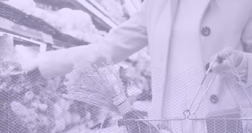 Person in coat placing items into a shopping basket while reaching for produce in a grocery store.