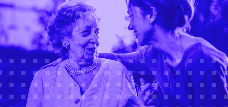 Elderly woman and younger woman share a warm, smiling moment outdoors, holding hands.