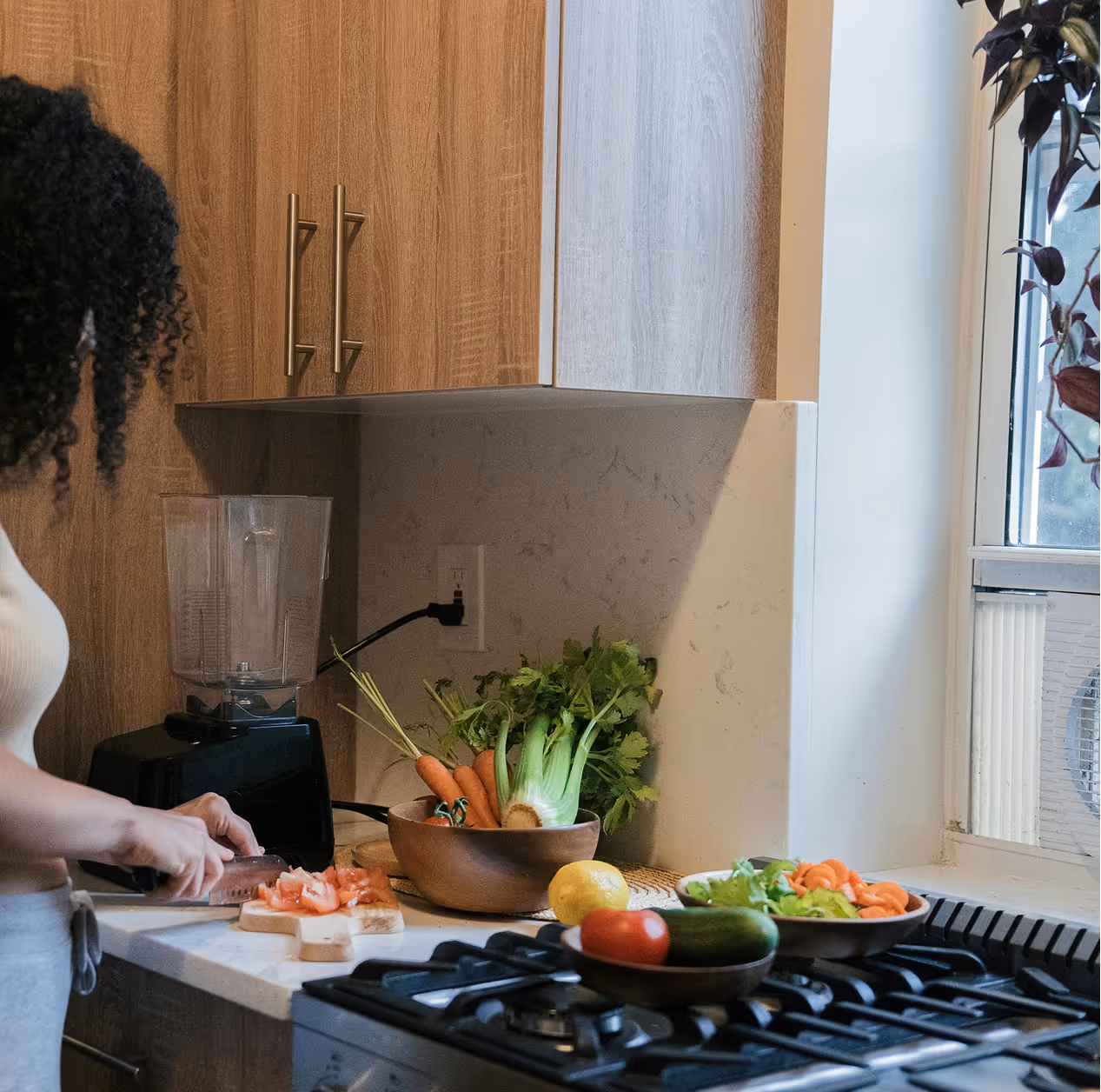 Person chopping tomatoes on a kitchen counter with vegetables and a stovetop nearby.