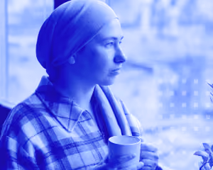 Woman wearing headscarf and plaid shirt holding a cup, gazing out a window with a blurred background.