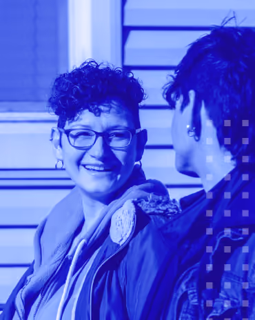 Two people outdoors, one smiling and wearing glasses, engaged in conversation.