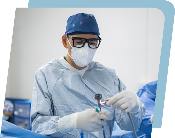 Surgeon wearing protective glasses, mask, gloves, and surgical gown performing a procedure with medical instruments.