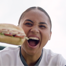 Person excitedly holding a sandwich close to the camera with mouth open wide.
