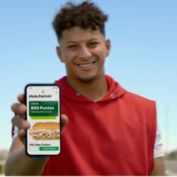 Smiling man in red hoodie holding a smartphone displaying 850 points and a sandwich offer from Subway.