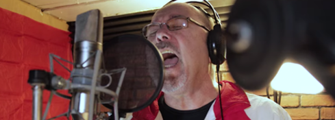 Man wearing glasses and headphones singing passionately into a microphone in a recording studio.