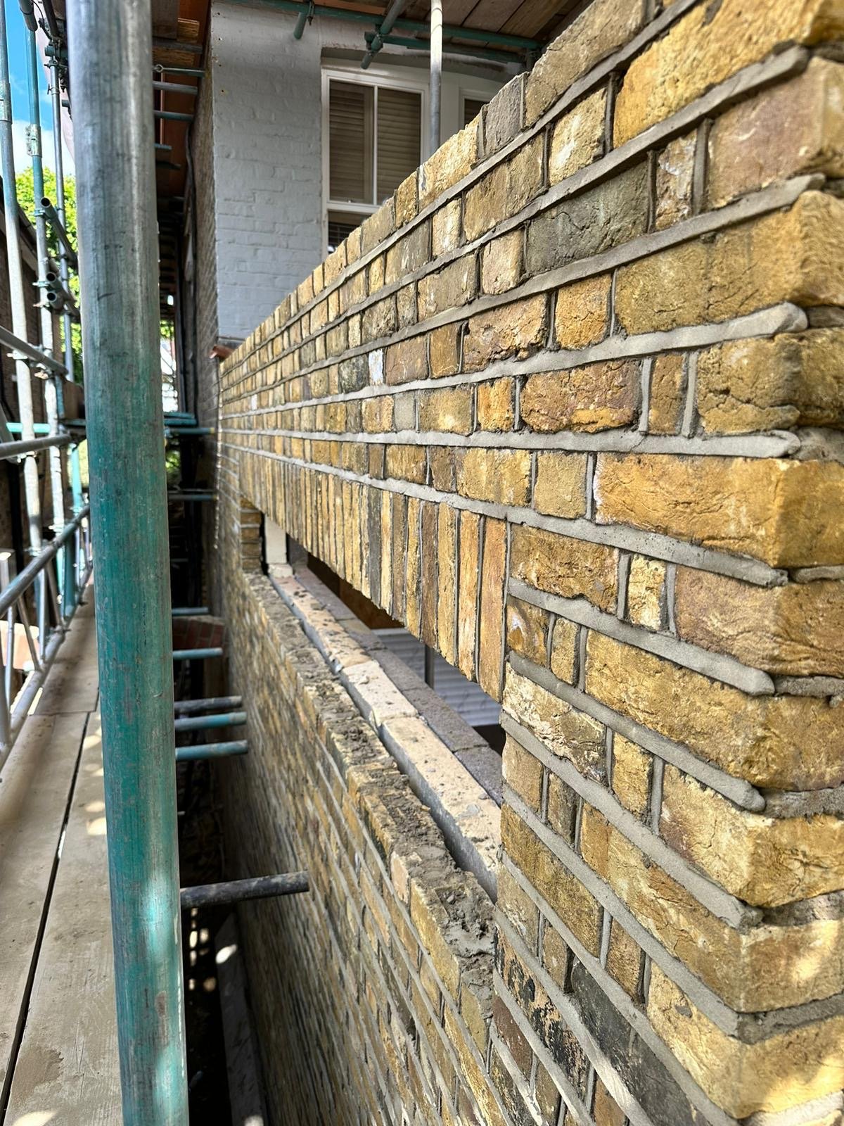 Close-up of newly constructed yellow brick wall on a building with metal scaffolding on the left side.