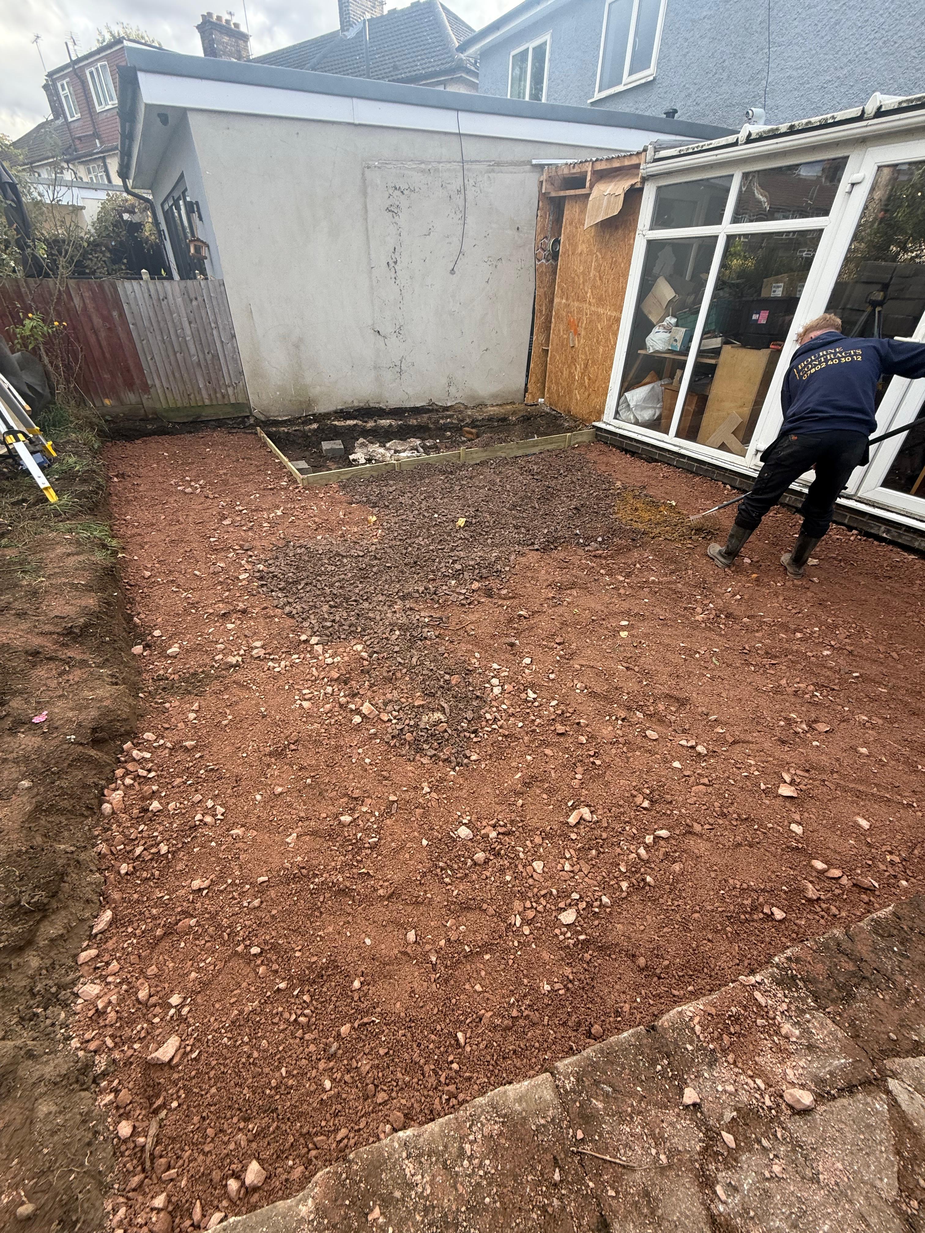 Person using a rake on a freshly leveled, gravel-covered backyard area next to a house with a glass door.
