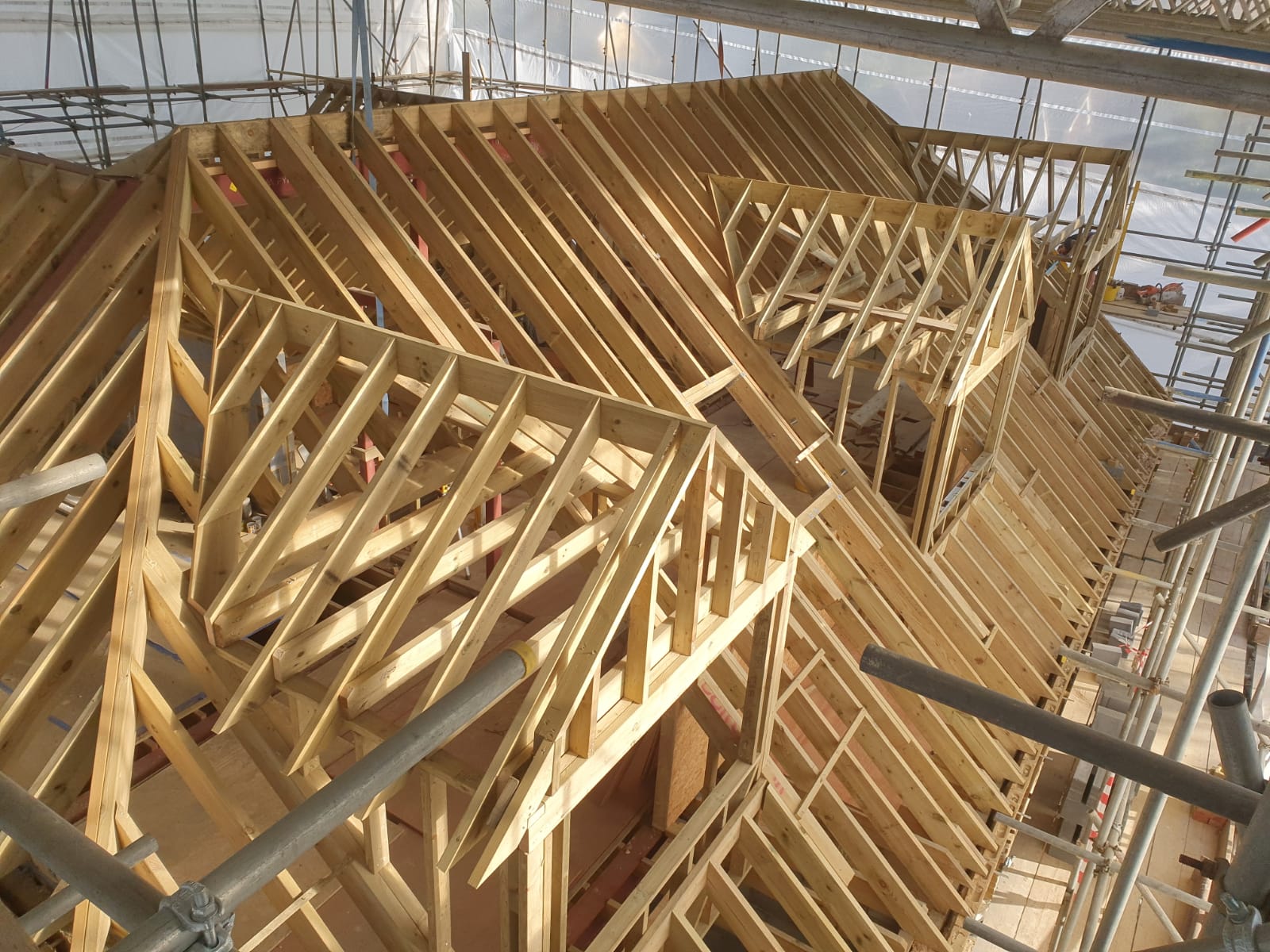 Wooden framework of a house roof under construction with scaffolding surrounding it.