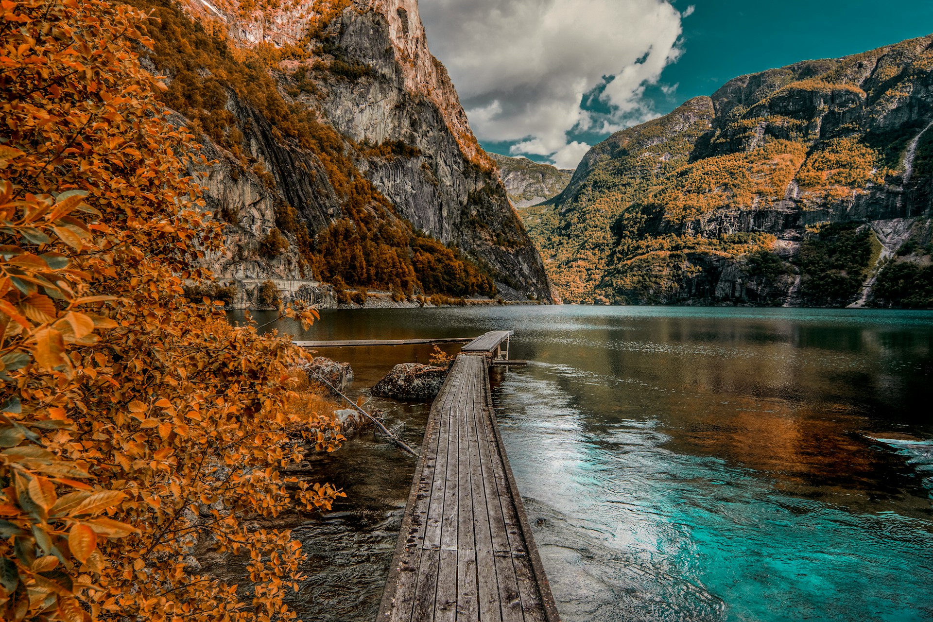 Scenic lake surrounded by mountains with autumn-colored trees and a wooden boardwalk. 