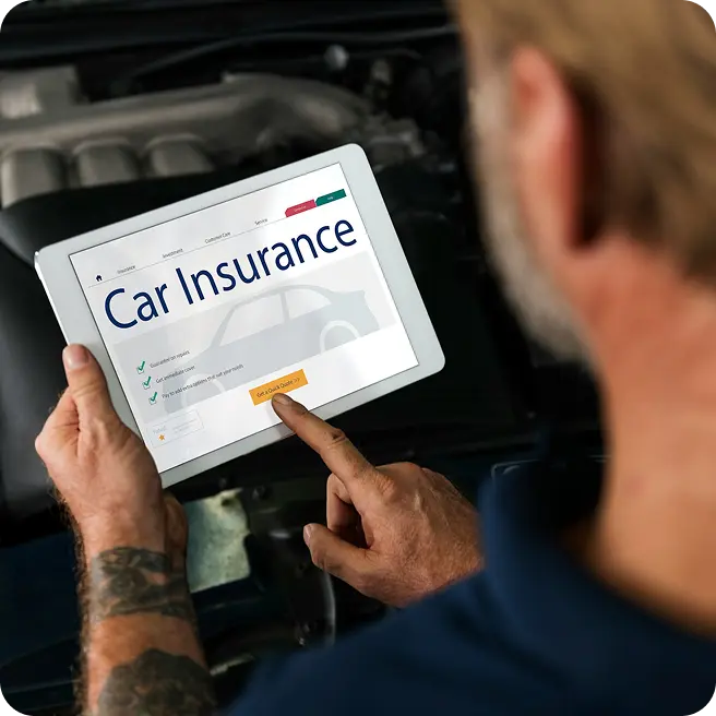 Man with tattooed arm using a tablet to browse a car insurance website.