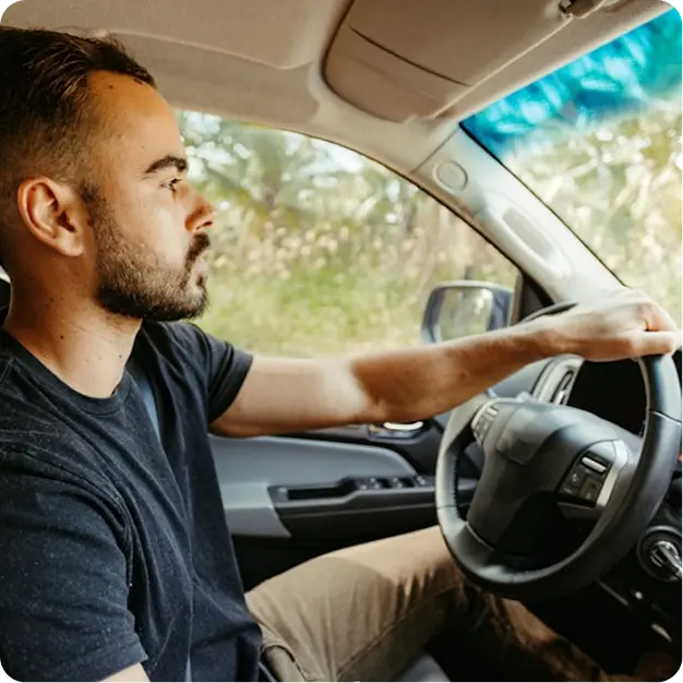 Man with a beard and mustache driving a car, looking focused ahead.