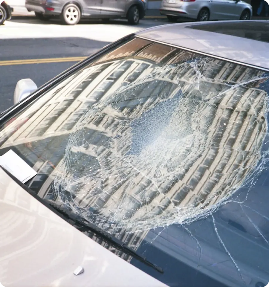 Car windshield with a large circular crack and shattered glass.