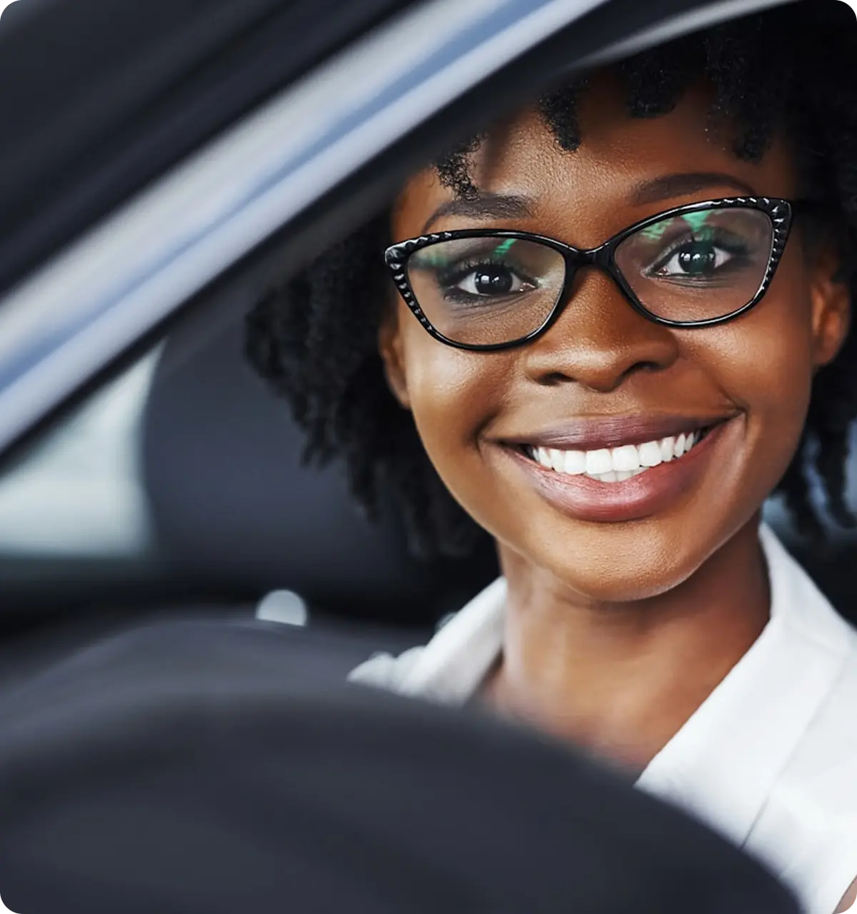 Smiling woman with glasses sitting in a car, visible through the steering wheel.