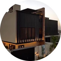 Modern two-story house with dark vertical slats on the upper level and warm interior lighting during dusk.