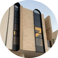 Modern beige building facade with tall black-framed arched windows and warm interior lighting.