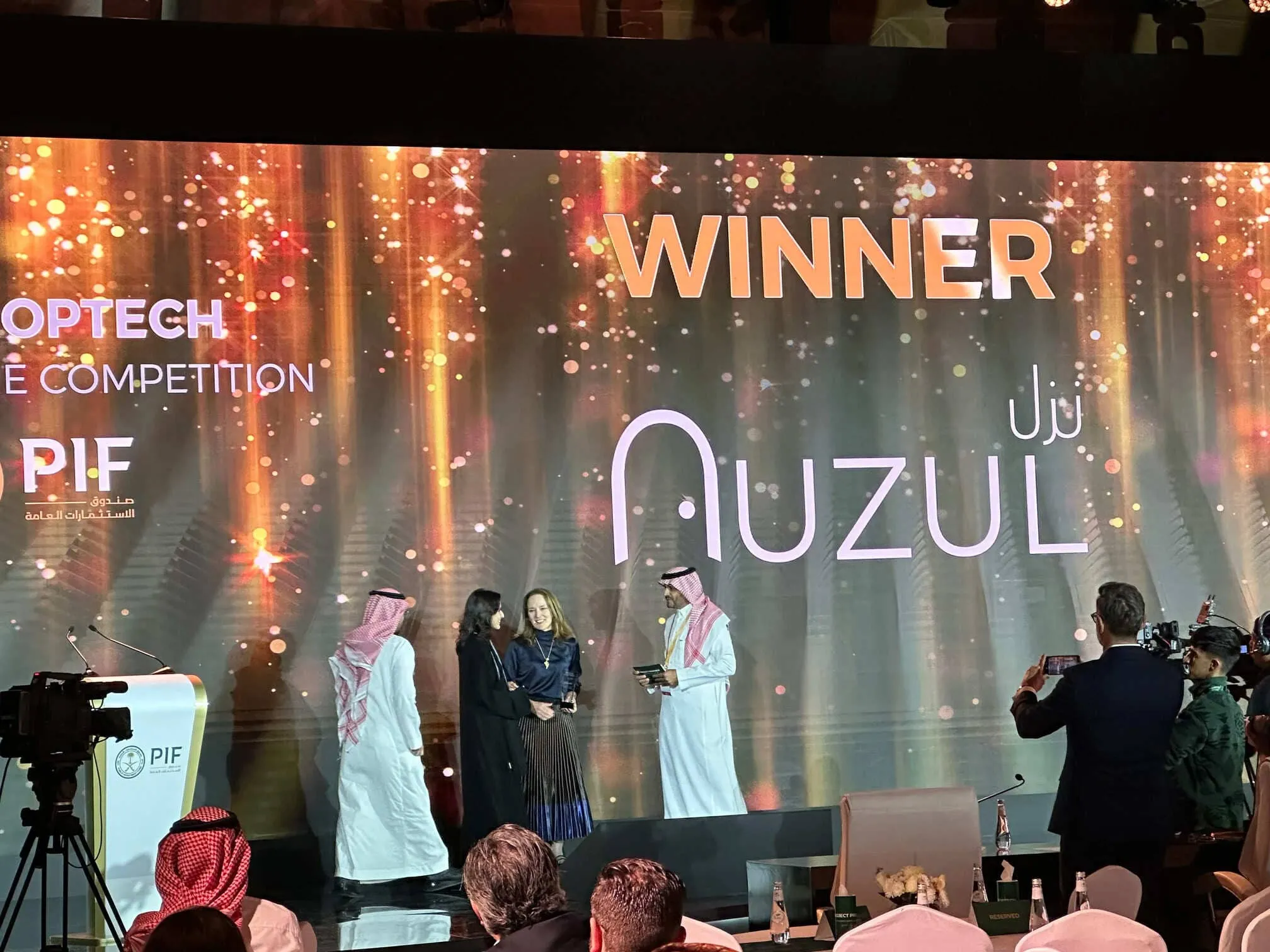 Award ceremony with people on stage and a large screen displaying 'WINNER AUZUL' and PIF logo in the background.