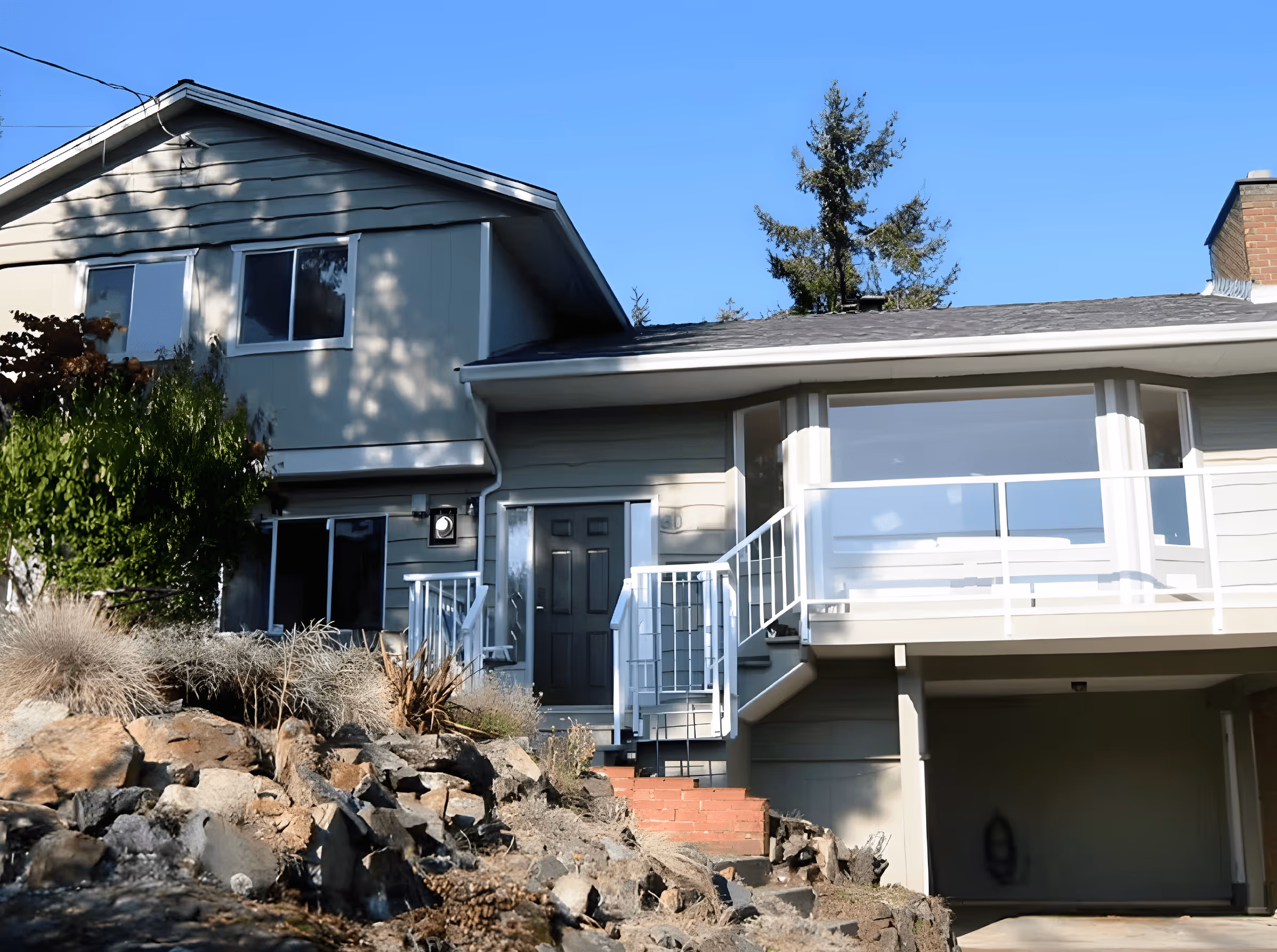 Two-story beige house with a front porch, white railings, and a garage beneath a clear blue sky.