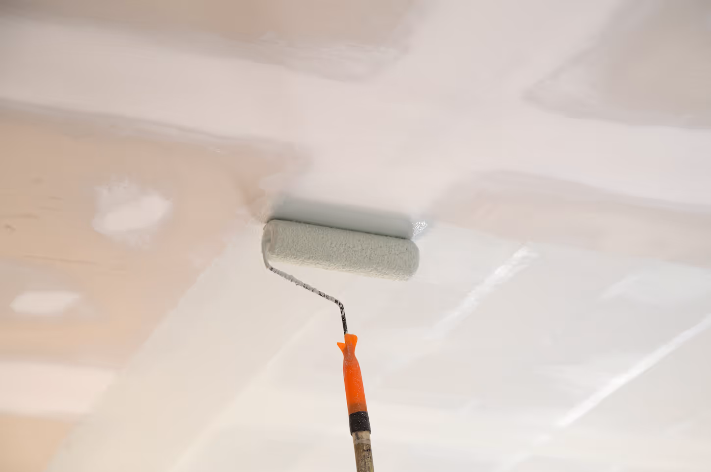 Paint roller applying white paint evenly on a ceiling.