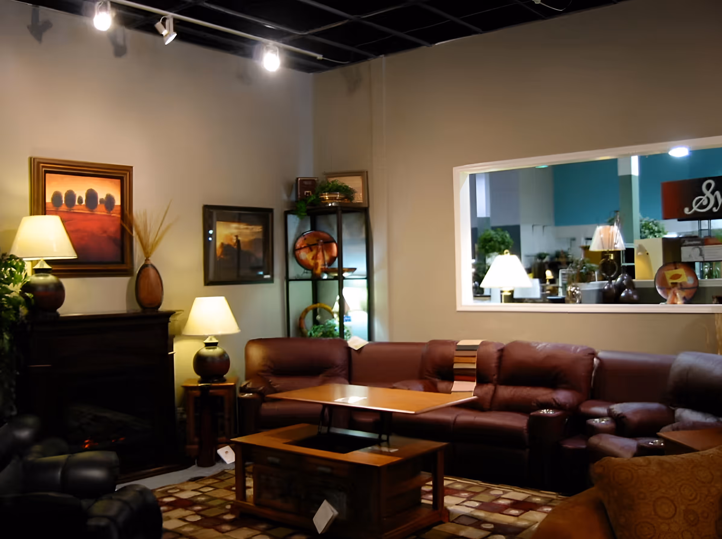 Cozy living room with dark leather sectional sofa, wooden coffee table, lamps, framed paintings, and an electric fireplace.