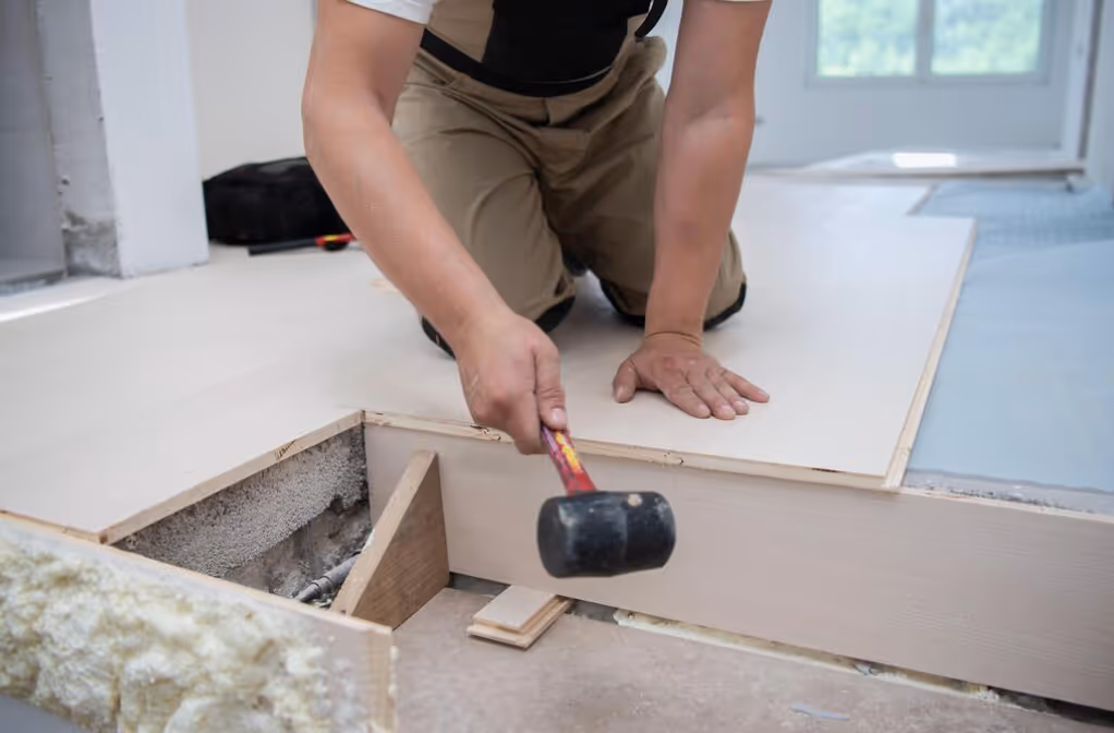 Man kneeling while installing wooden flooring using a rubber mallet.