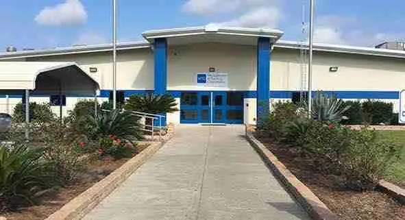 Edificio de entrada con camino de concreto flanqueado por jardines y arbustos, cielo azul con nubes. https://butlercohen.com/portfolio/iah-detention-center-polk-county/ 