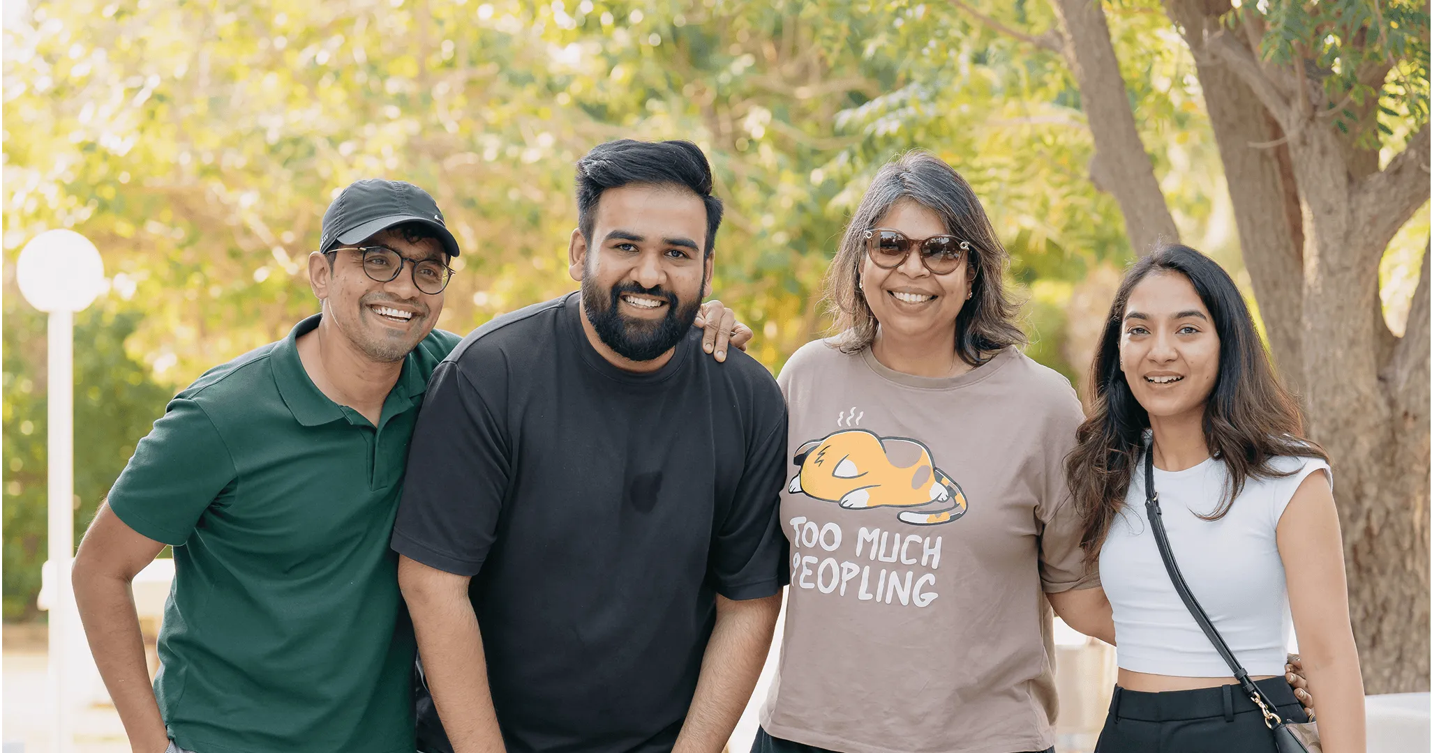 Four people posing outdoors with trees in the background.