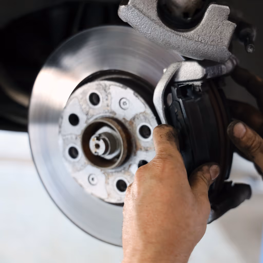 A Maxamy Mobile Autocare technician performing a detailed inspection of a car's brake disc and caliper assembly during a mobile service.