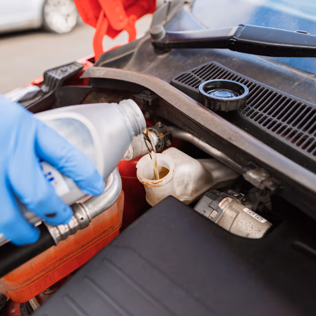 A Maxamy Mobile Autocare technician wearing blue gloves pours fresh brake fluid into the reservoir during a mobile maintenance visit.