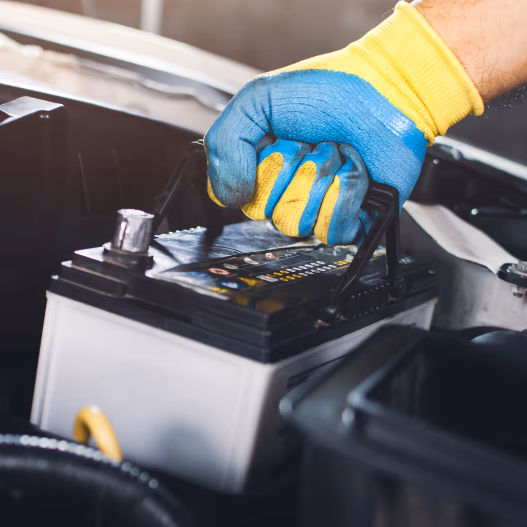 A mechanic from Maxamy Mobile Autocare lifts an old, worn car battery out of a vehicle's engine compartment during an on-site battery replacement.