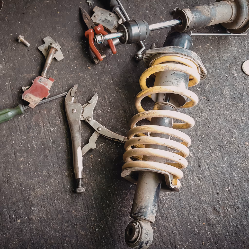 A removed, old shock absorber and a pair of pliers are shown on the ground, indicating a suspension repair is in progress.