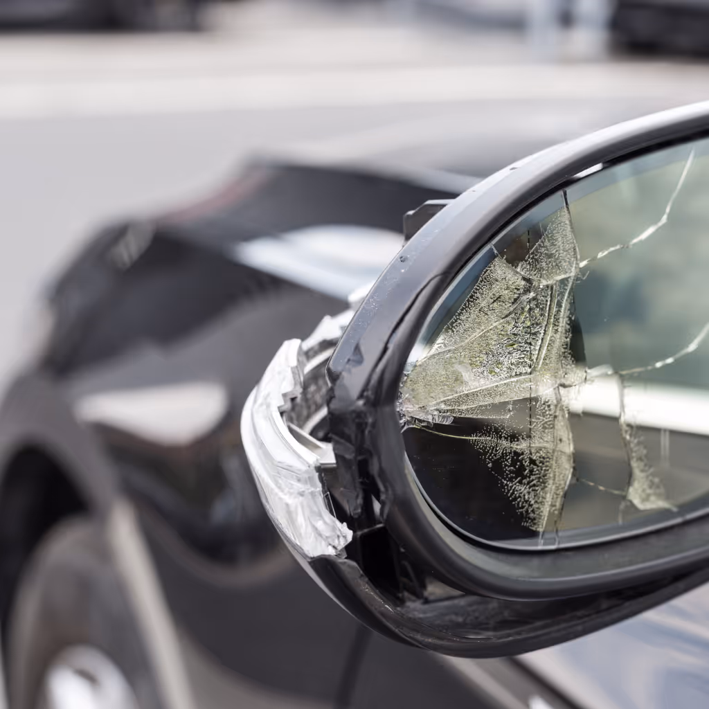 A close-up of a car's side mirror with shattered glass and a damaged housing, a common bodywork repair performed by Maxamy Mobile Autocare.