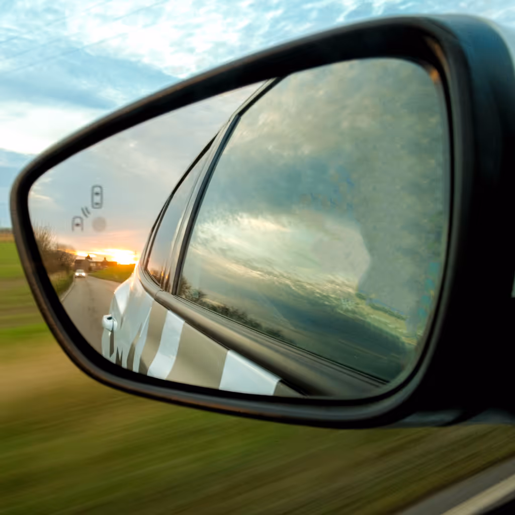 A close-up of a clean, undamaged side mirror reflecting a sunset and a country road, showcasing quality bodywork by Maxamy Mobile Autocare.